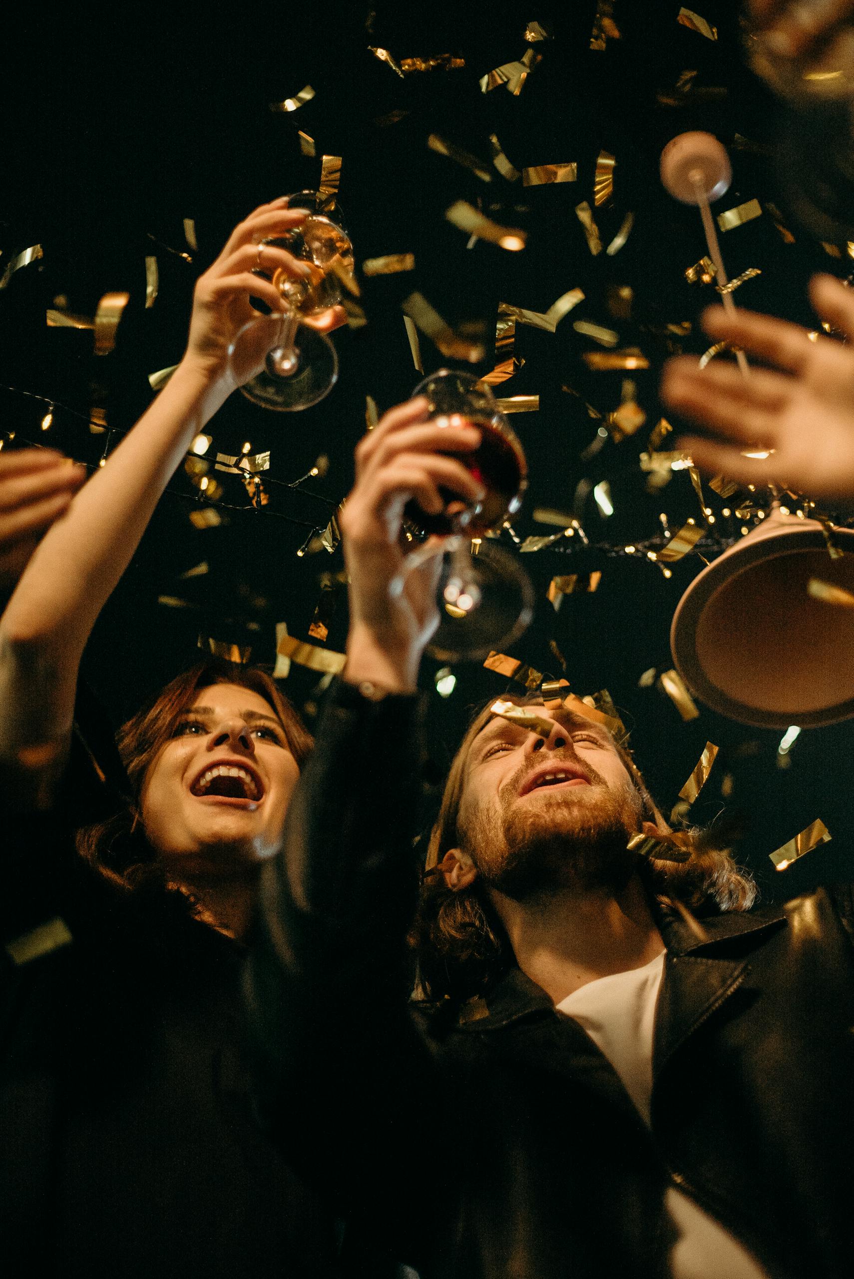 Group of friends enjoying New Year's Eve party with confetti and drinks.